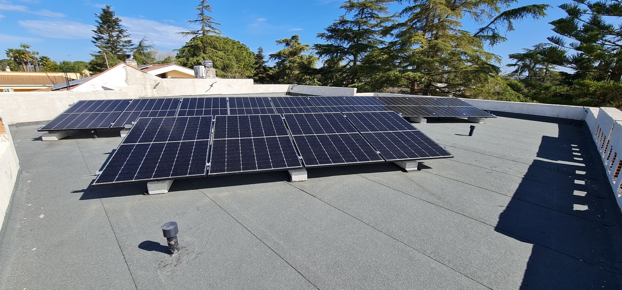 Grande impianto fotovoltaico su copertura piana circondata da alberi